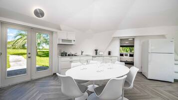 Une cuisine moderne avec une table de salle à manger ronde et des chaises blanches, un four à micro-ondes encastré et un réfrigérateur.