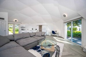Un loft moderno con un amplio sofá seccional gris, una mesa de centro de vidrio y vistas a un exuberante jardín a través de grandes puertas correderas.