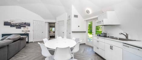 A modern kitchen with white cabinetry, a dining table with white chairs, and a grey sofa.