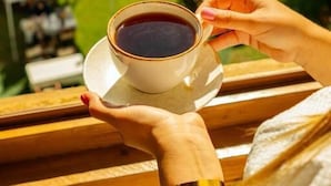 Une personne tenant une tasse de café sur un balcon donnant sur un jardin où sont installées des tentes blanches.