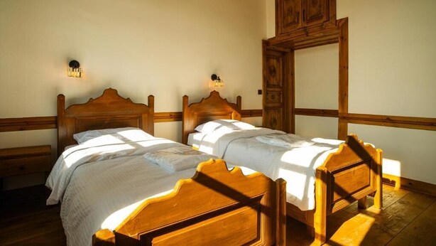 A room with two wooden beds, a wooden wardrobe, and wall-mounted light fixtures. - KASTAMONU MAVİ KONAK  (Kastamonu)