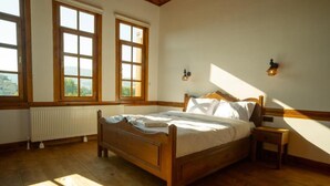 A bedroom with a wooden bed, two windows, a nightstand, and a radiator. - KASTAMONU MAVİ KONAK  (Kastamonu)