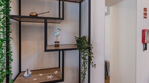 A modern interior with a geometric shelving unit displaying decorative items, a hanging plant, and a fire safety sign on the wall. - Casa Maria by LovelyStay (Trafaria)