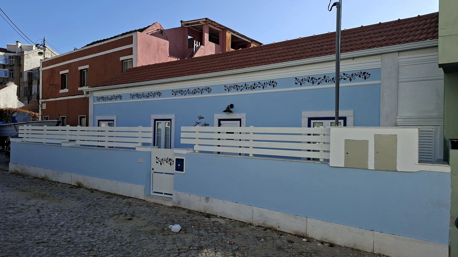 Ein Gebäude mit blauer Fassade, weißen Geländern und einem rot bedeckten Bau im Hintergrund.