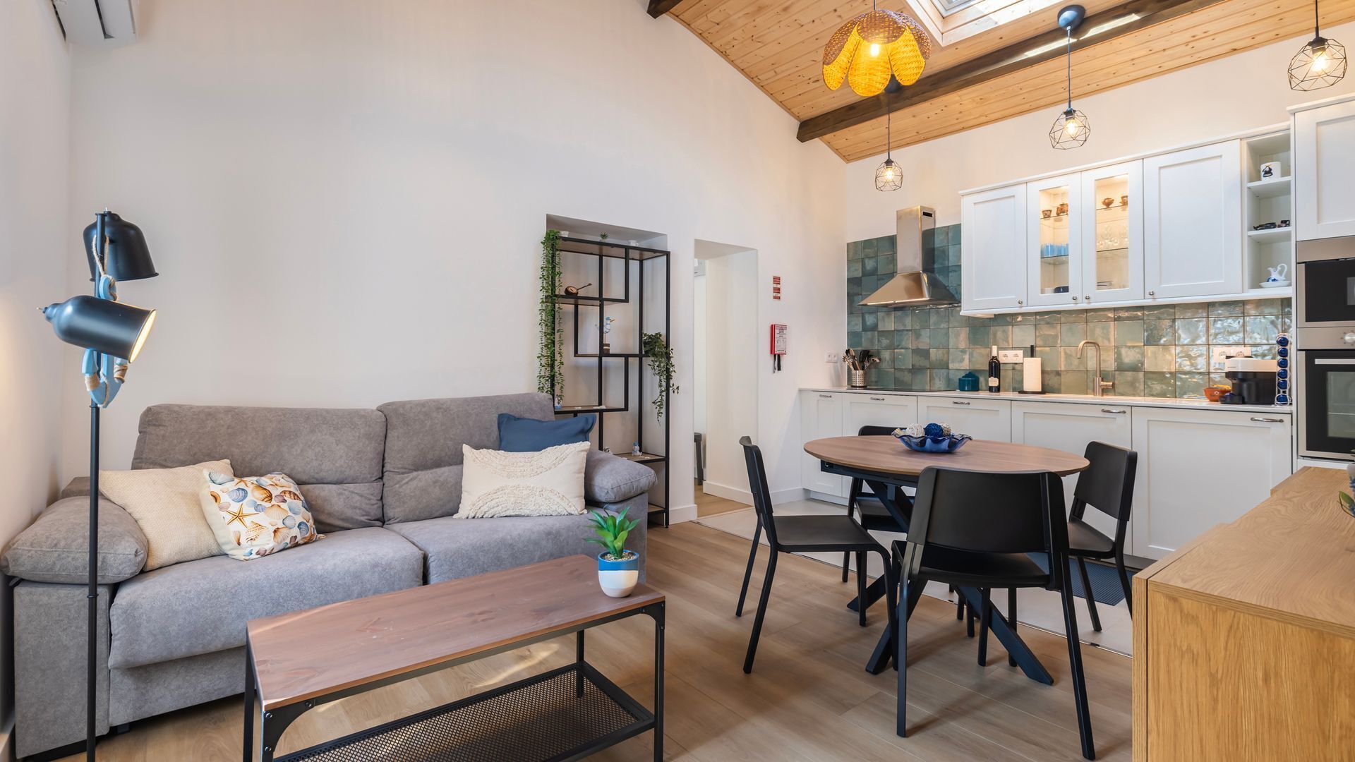 Ein modernes Wohnzimmer mit grauem Sofa, einem Holztisch und einem Essbereich mit Tisch und Stühlen.