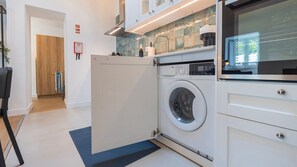 A modern laundry room with a front-loading washing machine, a drying machine, and a tiled backsplash. - Casa Maria by LovelyStay (Trafaria)