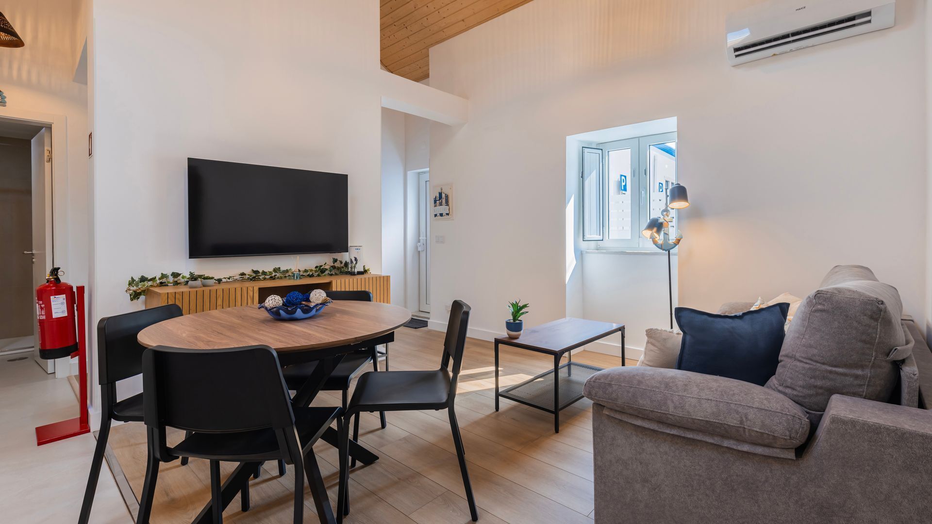 Ein modernes Wohnzimmer mit Flachbildfernseher, Essbereich mit Holztisch und Stühlen, Sofa und Fenster mit Blick.