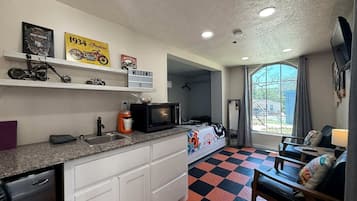 Habitación compacta con kitchenette, una cama, un sofá y una ventana con cortinas.
