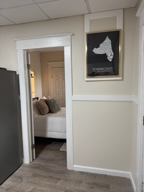 A hallway with a door leading to a bedroom, a framed map on the wall, and a wooden floor. - Cozy 2DR Apartment — Near Downtown Schenectady & Union College (Schenectady)
