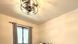 Ein Schlafzimmer mit einem Bett, einem Nachttisch, einer Lampe, einem Fenster mit Vorhängen und einer Deckenleuchte.