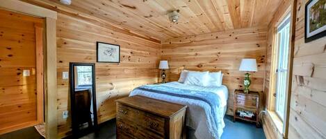 A wooden-paneled bedroom with a bed, bedside tables, and a dresser.