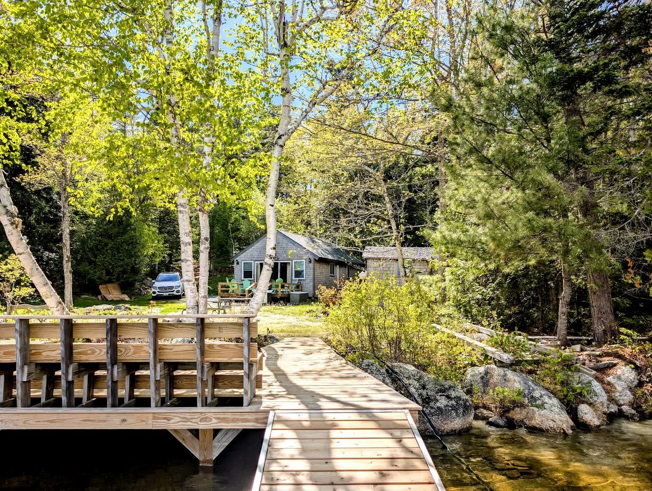 A wooden dock leading to a house surrounded by trees and a small stream.
