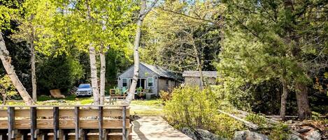 A wooden dock leading to a house surrounded by trees and a small stream.