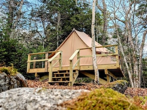 Eine Holzhütte mit einer Holzterrasse und einer Treppe, umgeben von Bäumen.