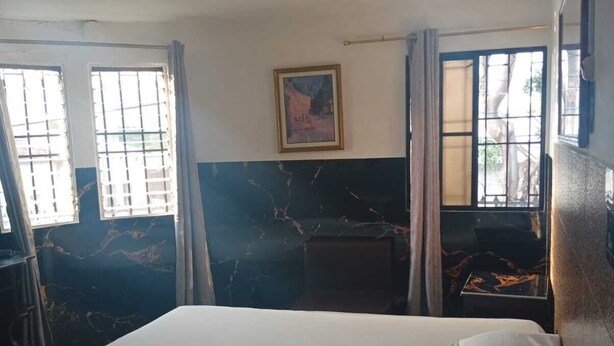 A hotel room with a bed, a small table, a chair, a painting on the wall, and a window with curtains. - Hotel California Santa Ana (Santa Ana)