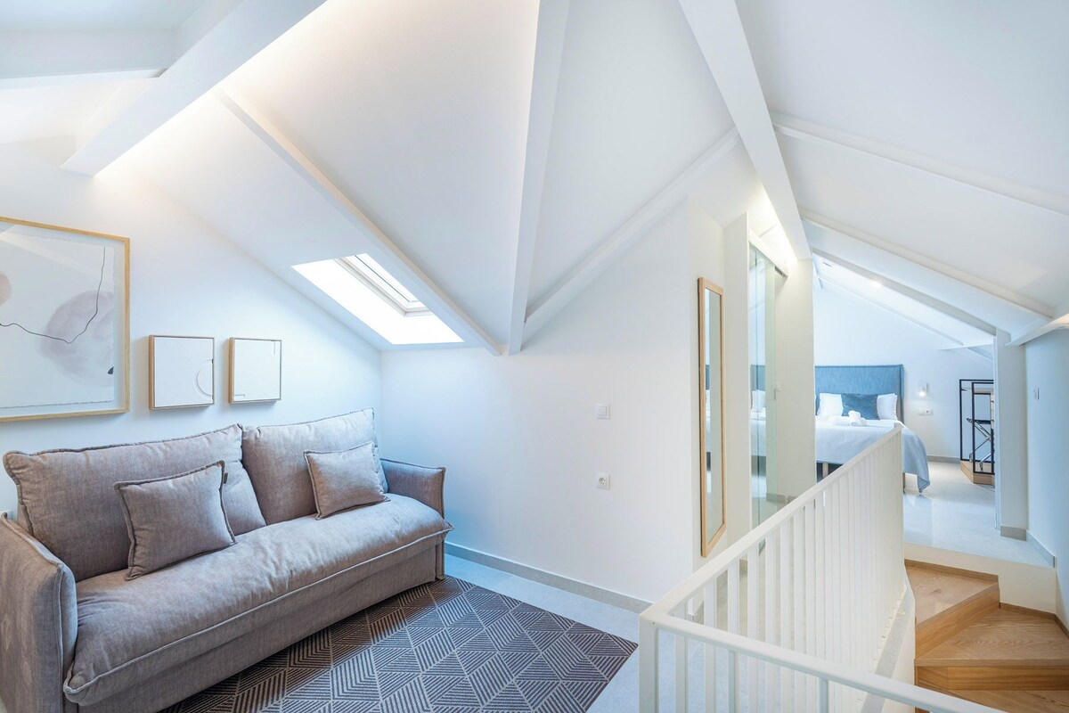 Ein modernes Schlafzimmer im Loft-Stil mit schrägem Dach, integriertem Bett, einer Treppe und Blick in den angrenzenden Raum.
