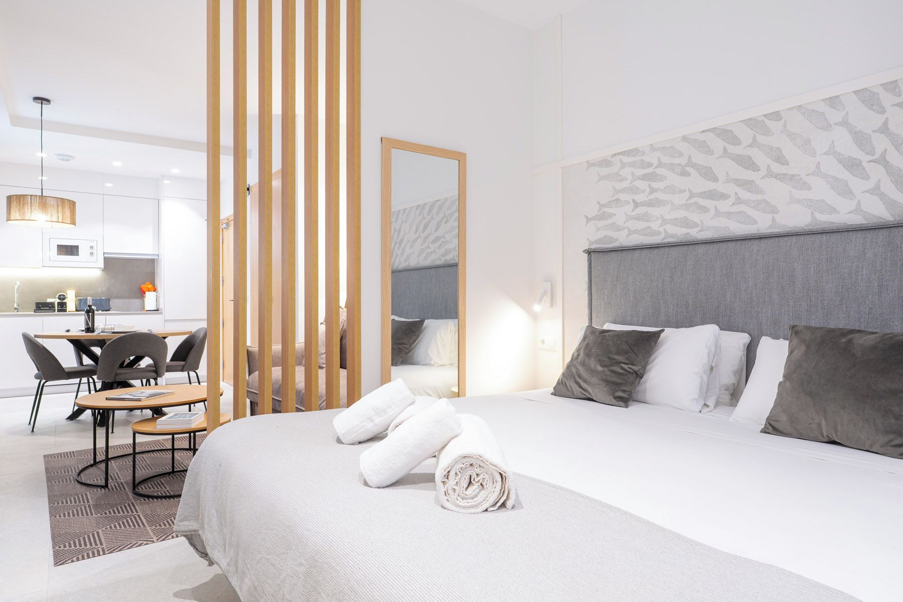 Une chambre d’hôtel moderne avec un grand lit, un coin repas avec des chaises, une cuisine en arrière-plan et un grand miroir.