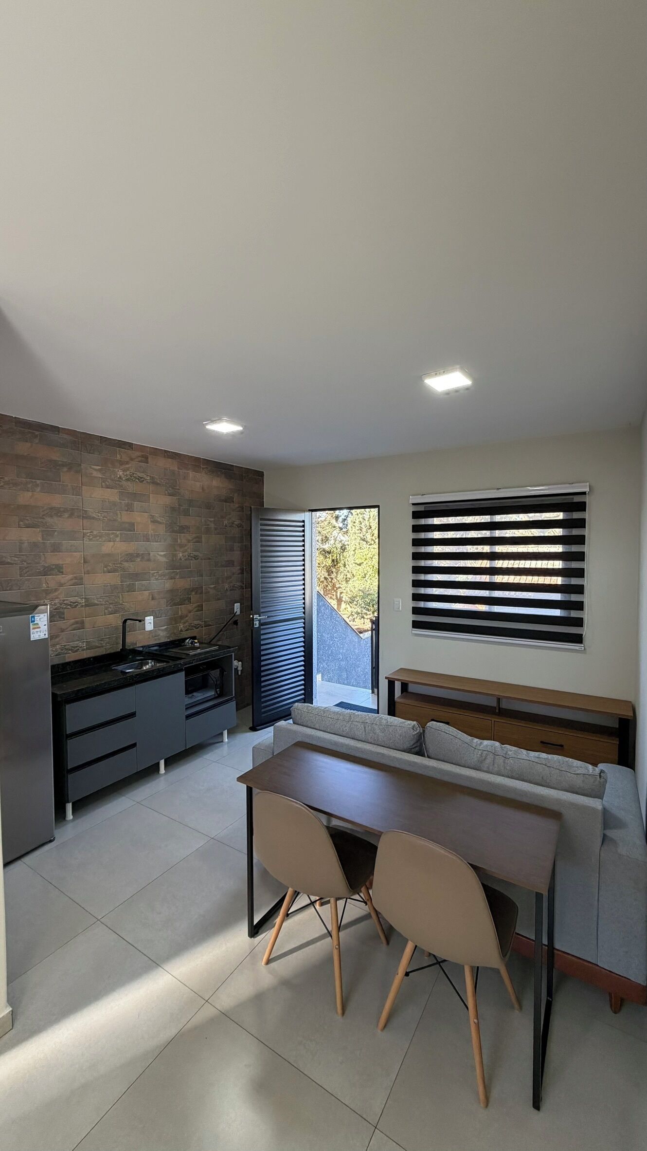 A modern kitchen with a built-in oven, a dining area with a table and chairs, and a large window with blinds.