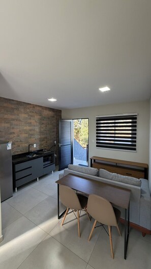 Una cocina moderna con horno empotrado, zona de comedor con mesa y sillas, y un amplio ventanal con persianas.