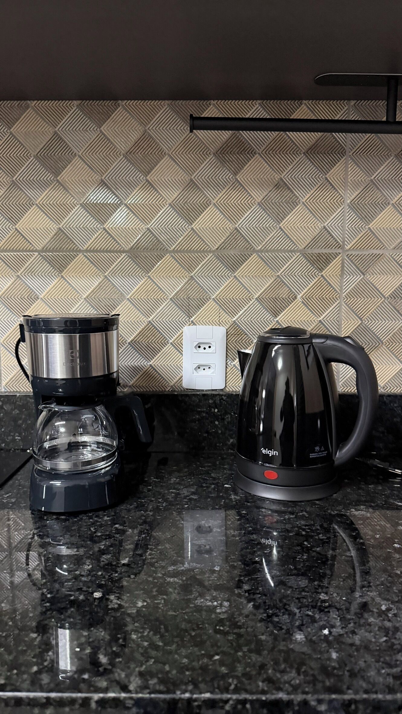 Un comptoir de cuisine avec une machine à café et une casserole, une prise électrique et un pare-éclaboussures à motifs.