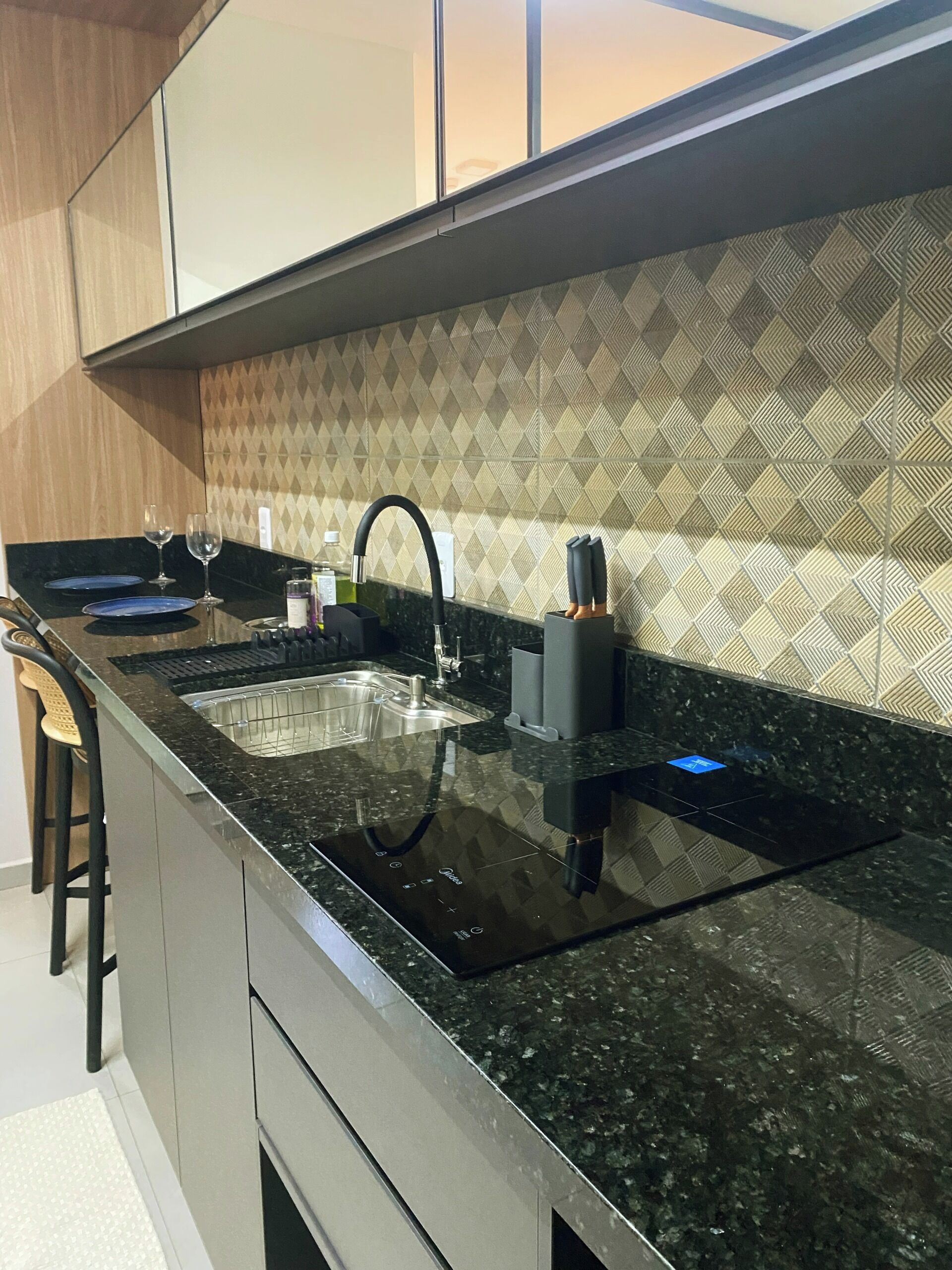Cozinha moderna com bancada de granito preto, pia de aço inoxidável e painel de fundo padronizado.