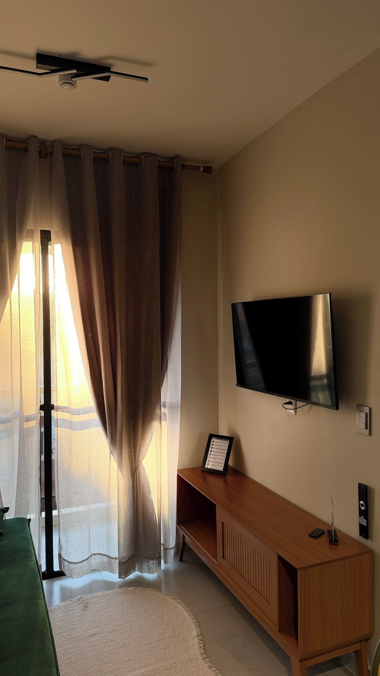 A room with a flat-screen TV mounted on the wall, a wooden console table, and a large window with curtains.