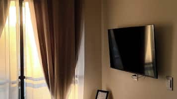 A room with a flat-screen TV mounted on the wall, a wooden console table, and a large window with curtains.