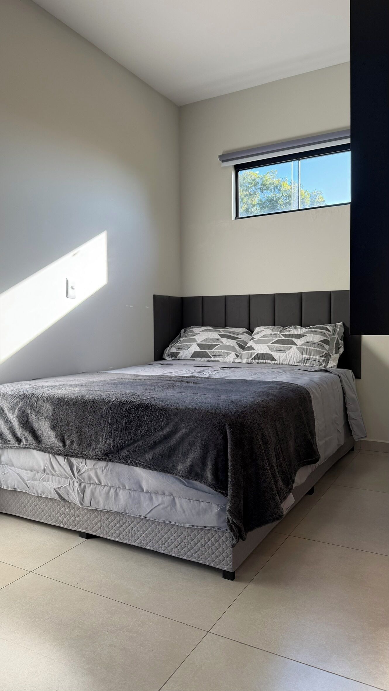 Un dormitorio con cama, ventana y una lámpara en la pared.