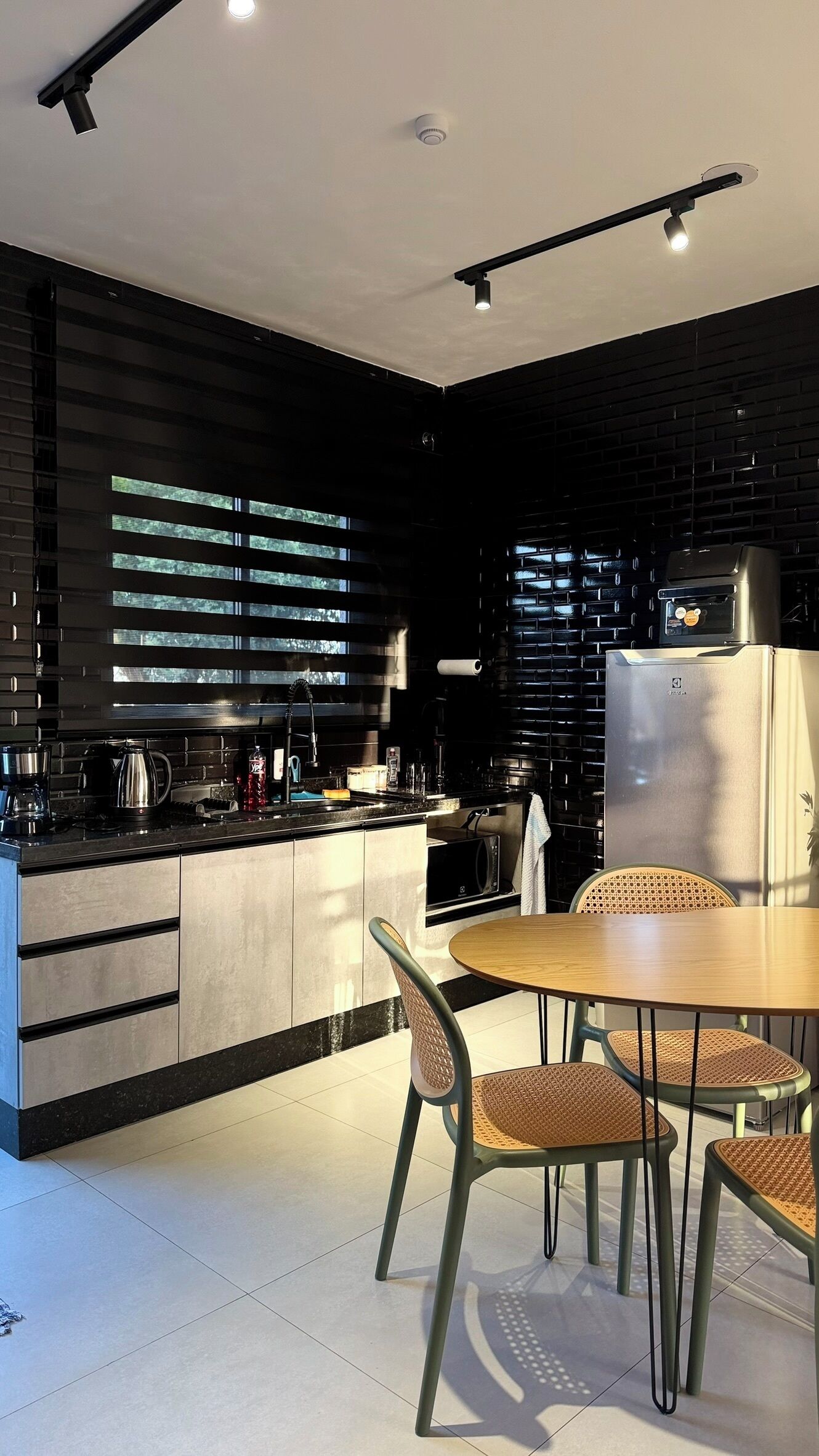 A modern kitchen with a central island, black cabinetry, and a dining area with rattan chairs.