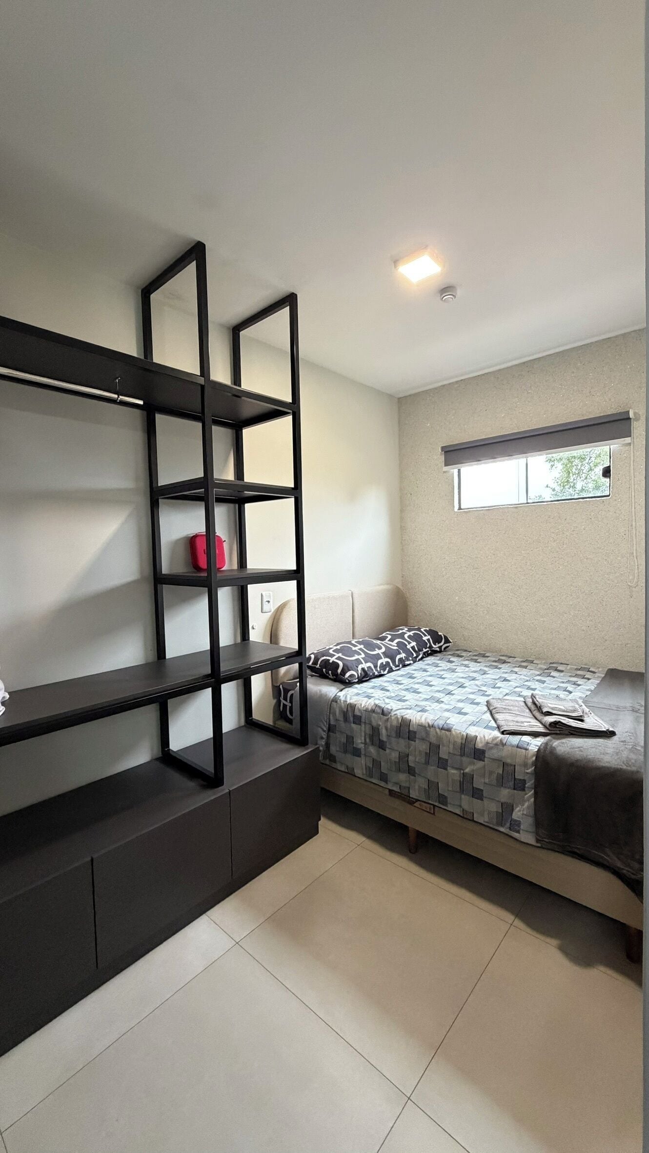 A bedroom with a bed, a built-in shelf unit, and a window.