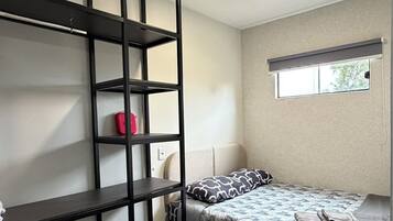A bedroom with a bed, a built-in shelf unit, and a window.