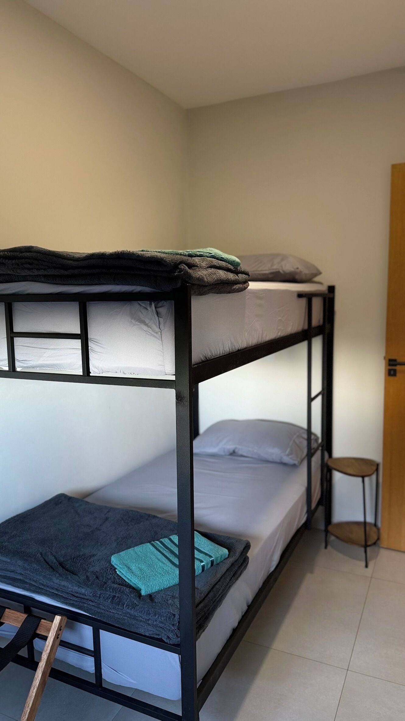 A bunk bed with a wooden ladder, a small stool, and a door in the background.