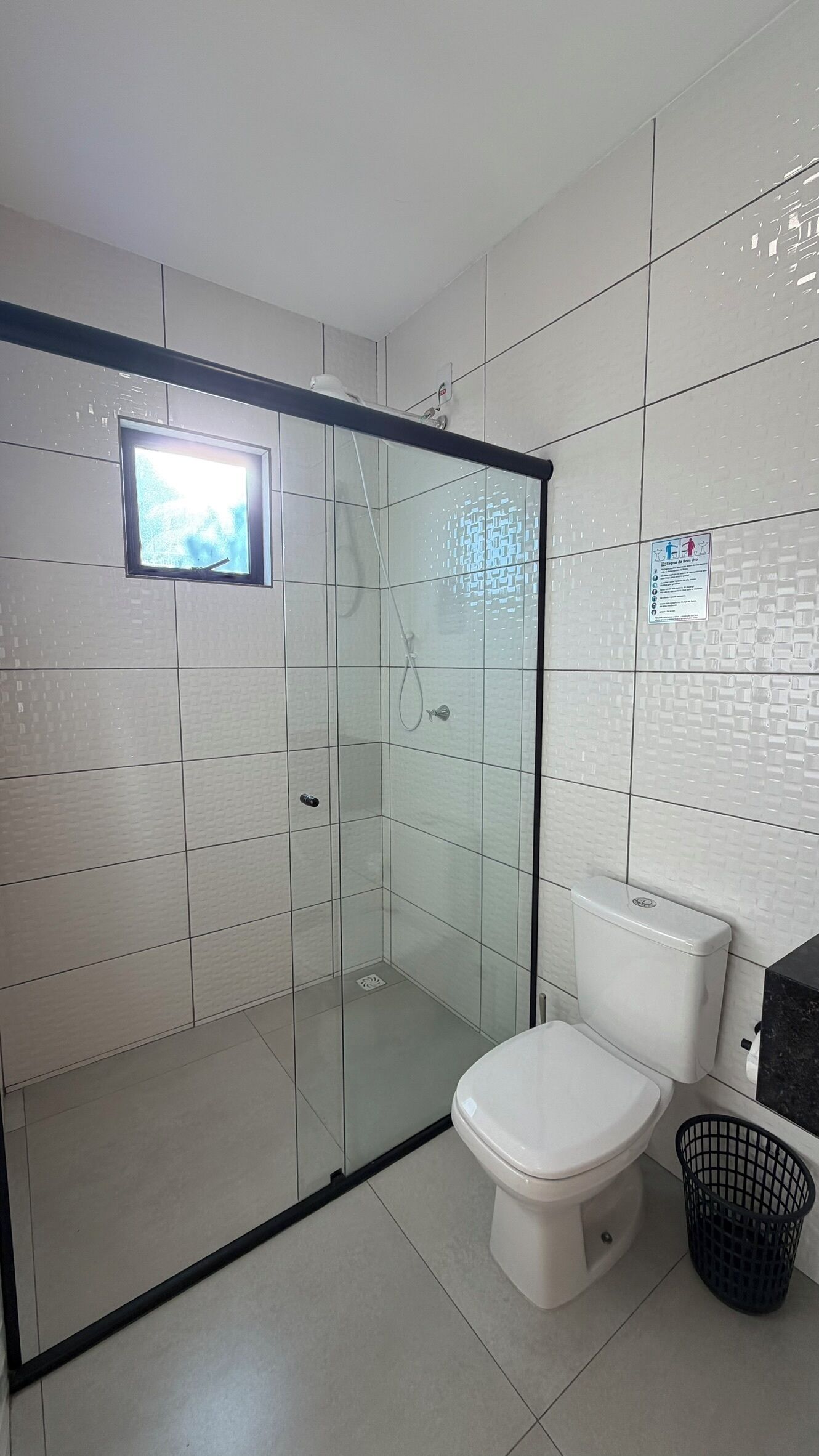 Un baño moderno con ducha envuelta en vidrio, inodoro y contenedor de basura.