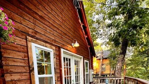 A wooden cabin with a deck, a table with chairs, and a door.