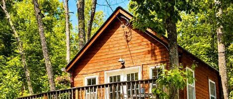 Una cabaña de madera con balcón, rodeada de árboles.