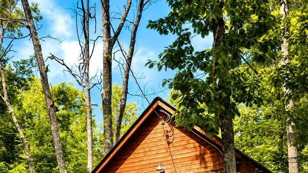 A wooden cabin with a balcony, surrounded by trees.