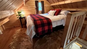 A cozy wooden cabin bedroom with a bed, a small bedside table, and a window.