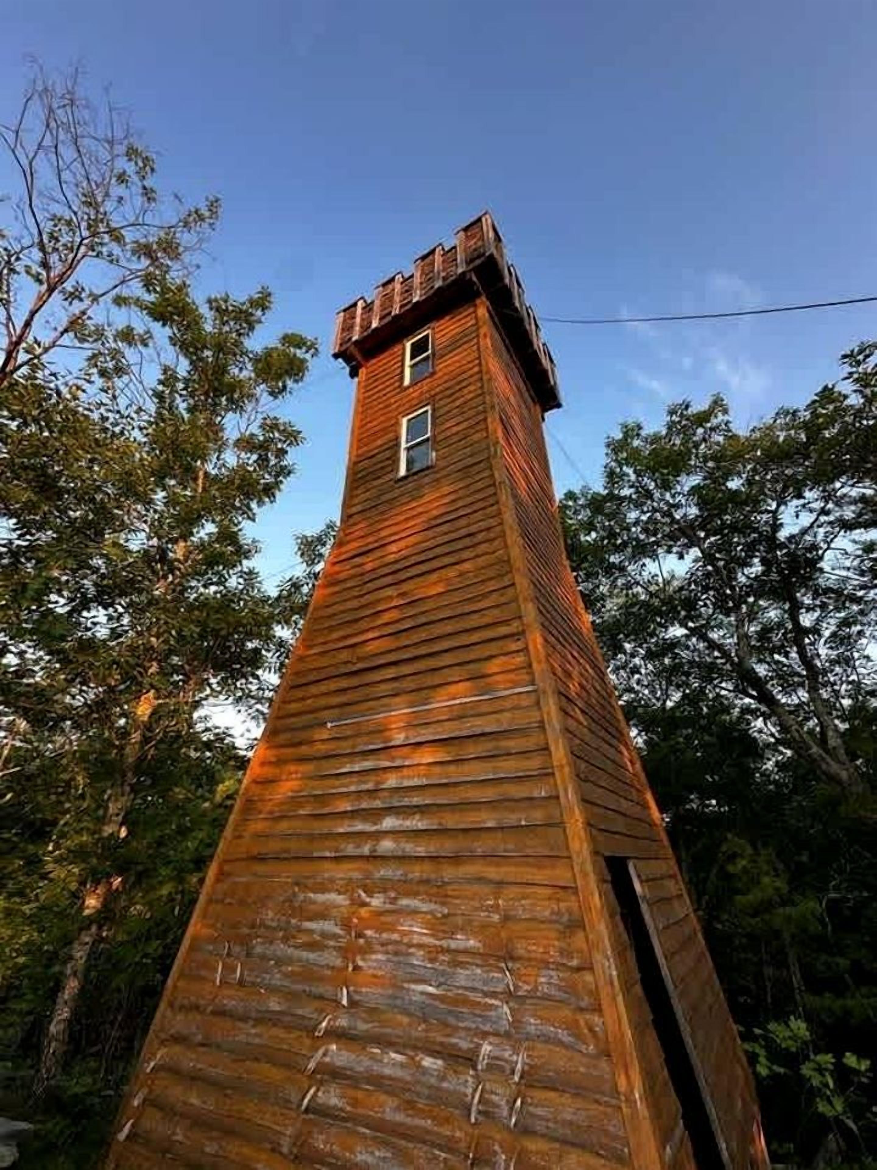 A tall wooden structure with a small window at the top, surrounded by trees.