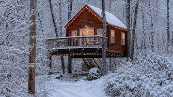 Une cabane en bois dotée d’un balcon, entourée d’arbres couverts de neige.