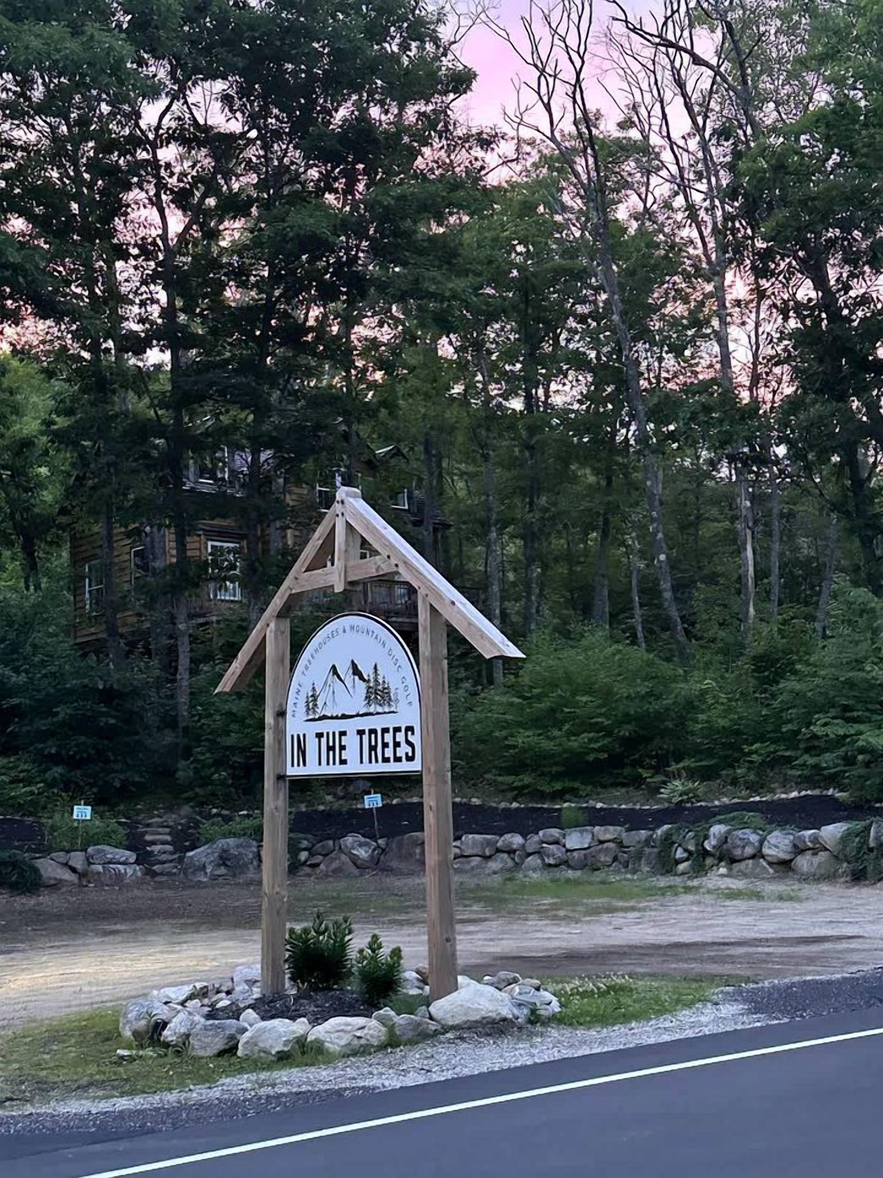 A wooden sign with the text 'IN THE TREES' and a mountain graphic, indicating a mountain-related attraction.