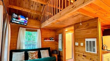 A wooden cabin interior with a loft bedroom, a sofa, a rug, and a television.