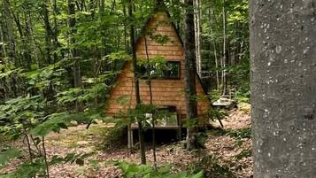 Una pequeña estructura de madera con forma triangular en un área boscosa.