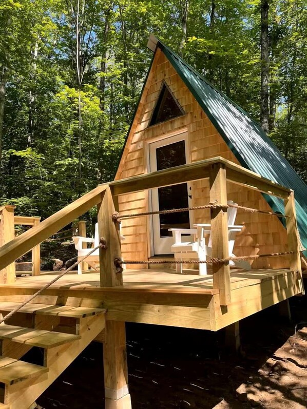 Una cabaña de madera con techo verde y una terraza, con una escalera que lleva a la entrada.