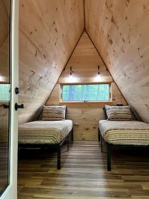 A room with two beds, wooden walls, a sloped ceiling, and a window. - Scenic Off-Grid A-Frame with Private Fire Pit near White Mountain National Forest, Stoneham, Maine (Stoneham)