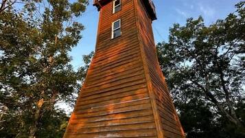A tall wooden tower with a small window at the top, surrounded by trees.