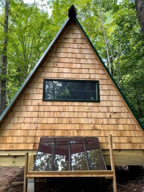 Una cabaña de madera con techo triangular, una ventana y una puerta con marco de ventana.