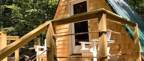 A wooden cabin with a green roof, a wooden deck, and a staircase leading to the entrance.