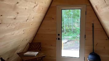Un intérieur en bois avec une porte donnant sur une vue de la forêt, une petite table et une poubelle.