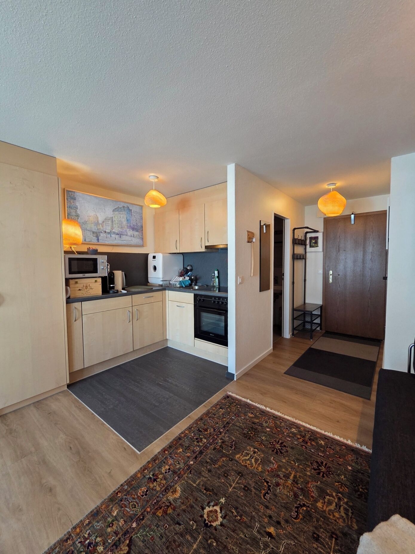 Une cuisine moderne avec des meubles en bois, un four à micro-ondes et une cuisinière. Il y a un tapis sur le sol et un tableau au mur.