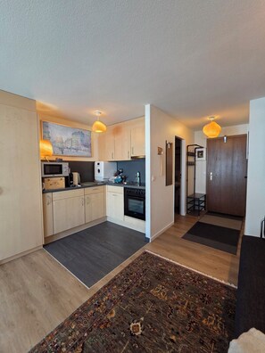 A modern kitchen with wooden cabinets, a microwave, and a stove. There is a rug on the floor and a painting on the wall.